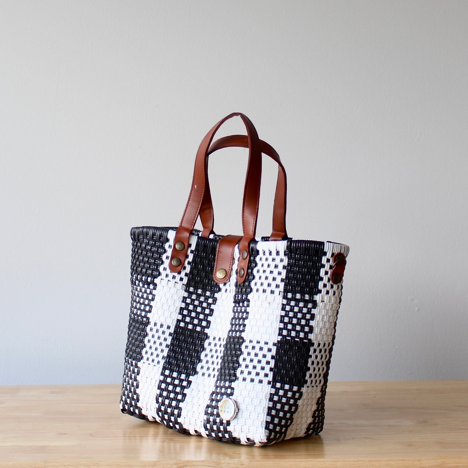 Black and white checkered tote bag with brown leather straps on a wooden surface.