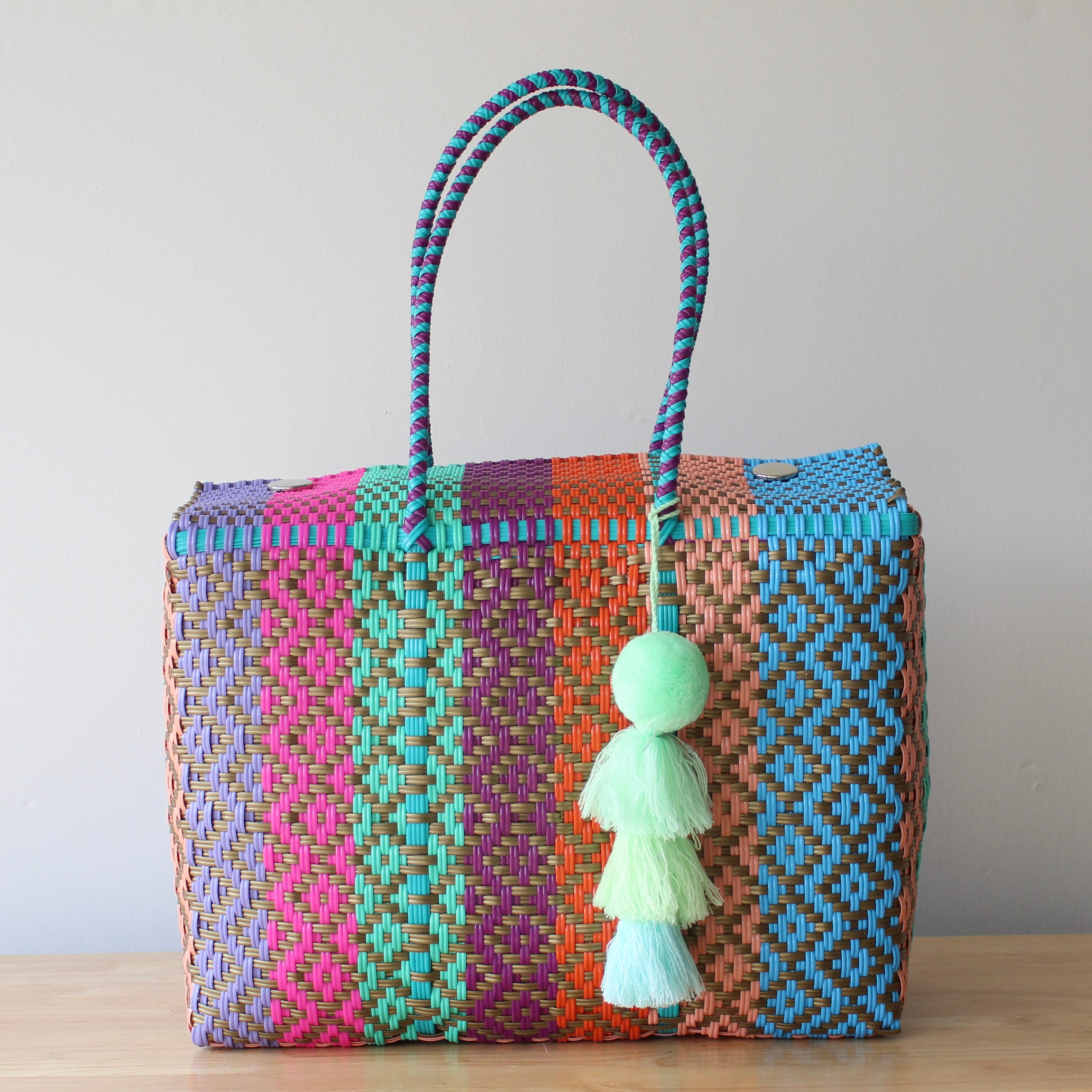 Colorful woven handbag with a tassel on a wooden surface and light gray background