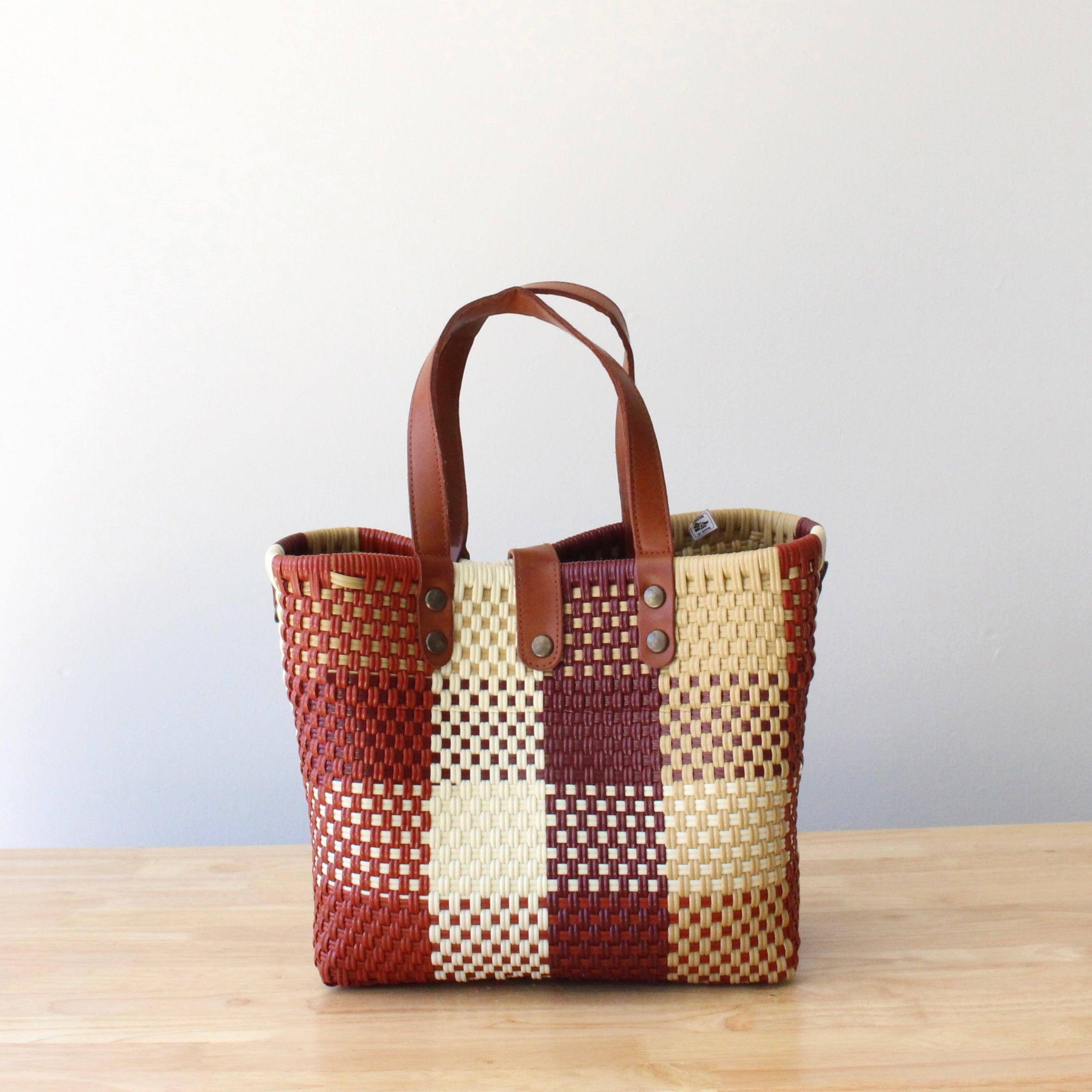 Handmade recycled plastic purse with brown leather handles, crafted by artisans in Mexico.