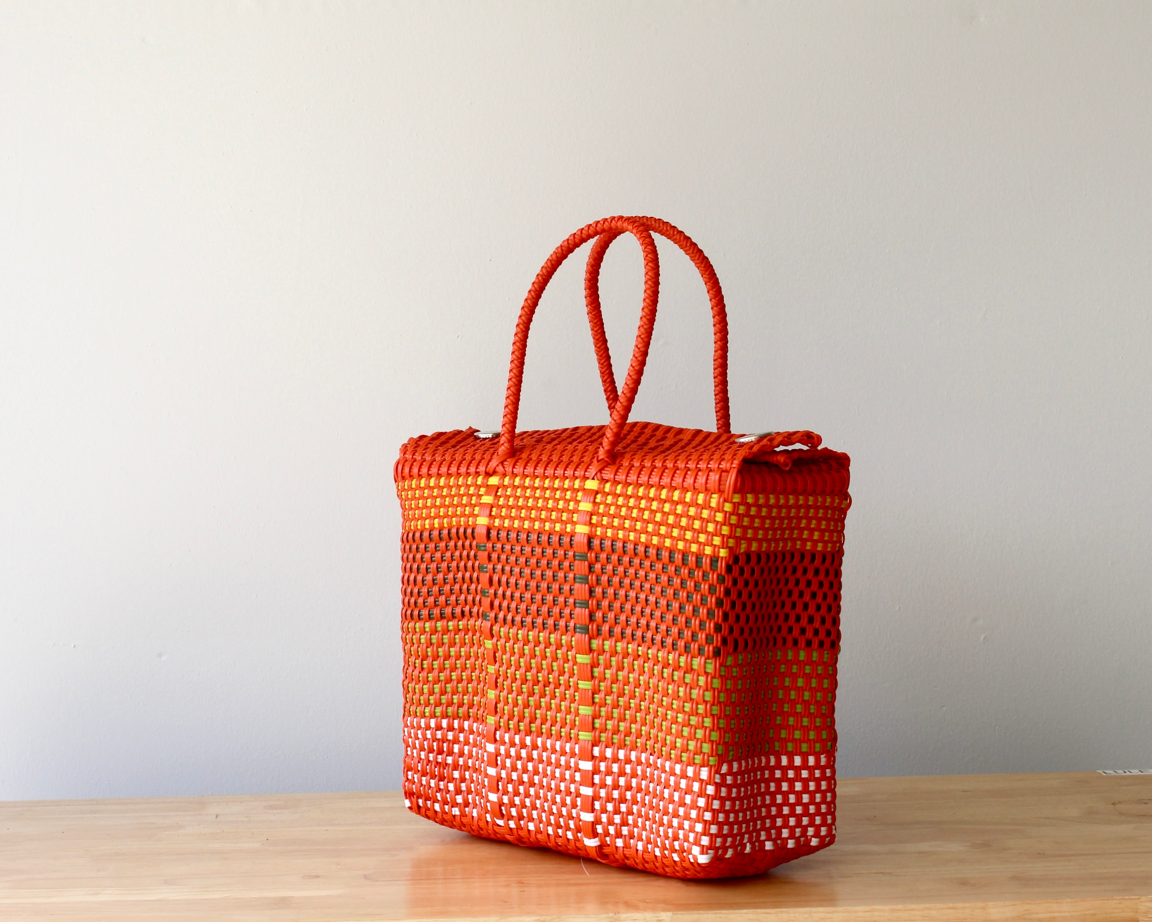 Woven orange bag with checkered pattern on a wooden surface and light gray background
