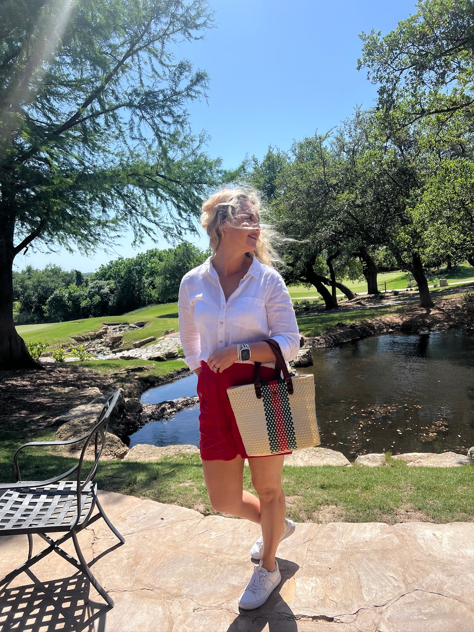Woman standing outdoors by a pond with trees and grass in the background
