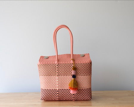 Woven handbag with a colorful tassel on a wooden surface and light gray background