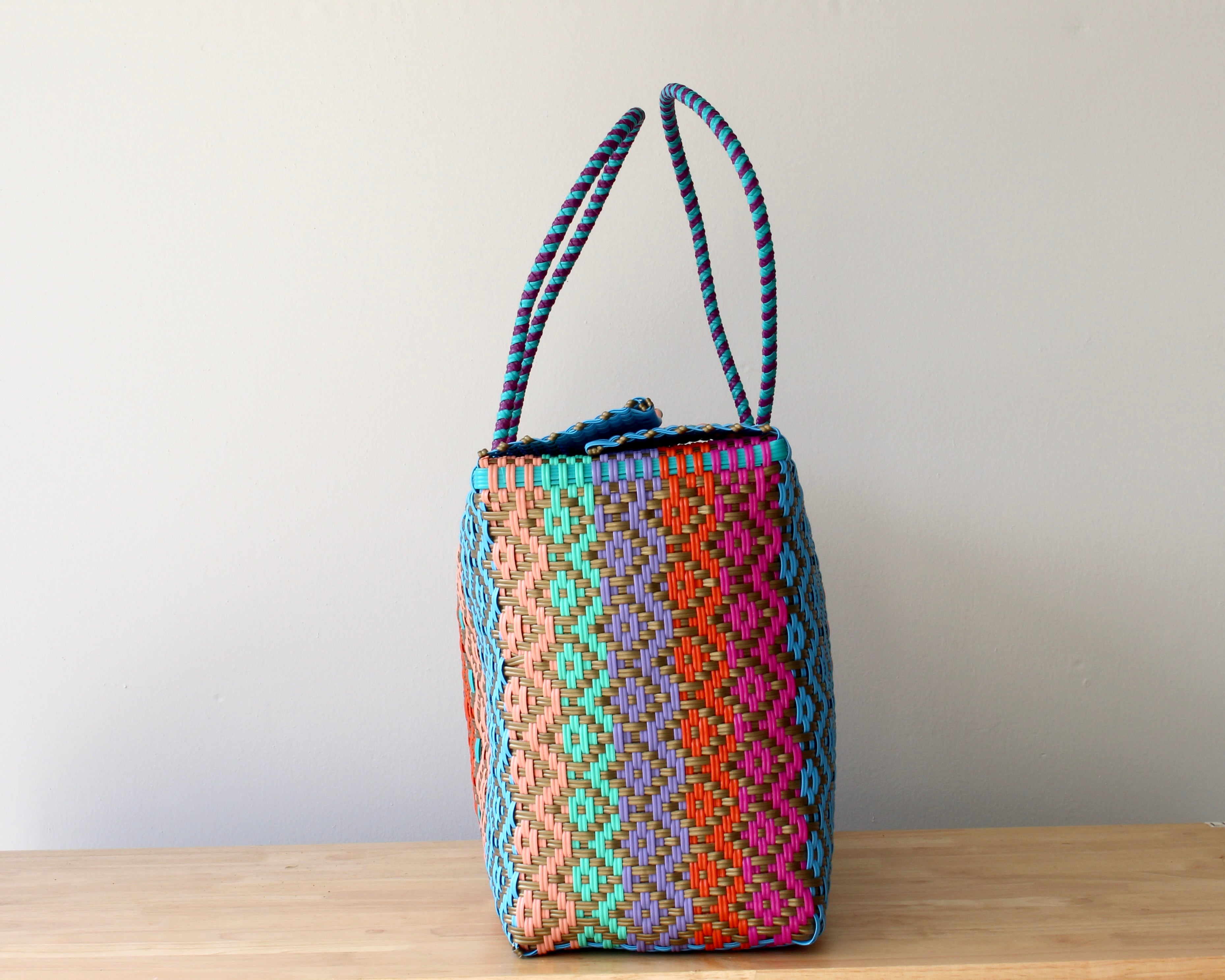 Colorful woven bag with patterned handles on a wooden surface against a plain background