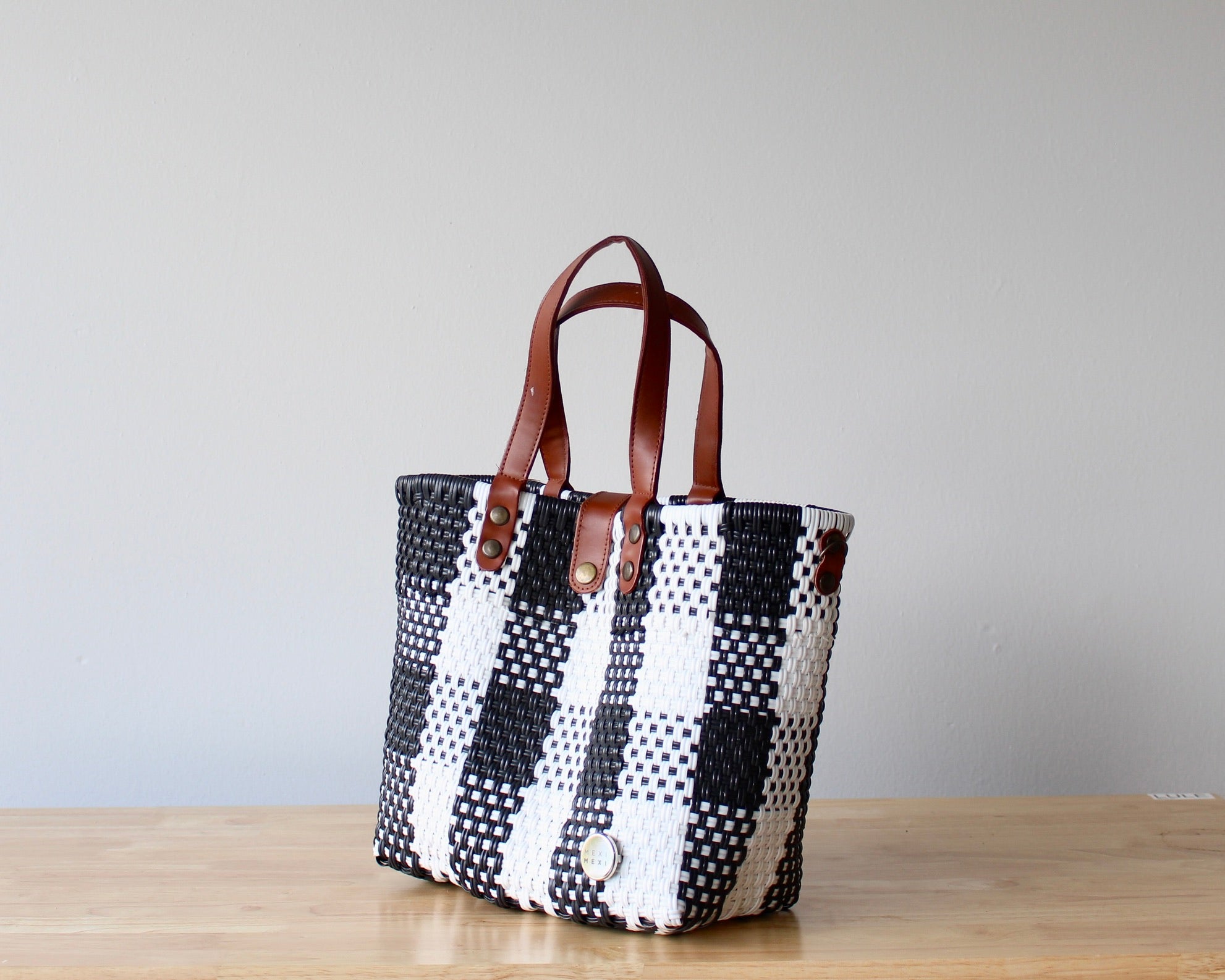 Black and white checkered tote bag with brown leather straps on a wooden surface.