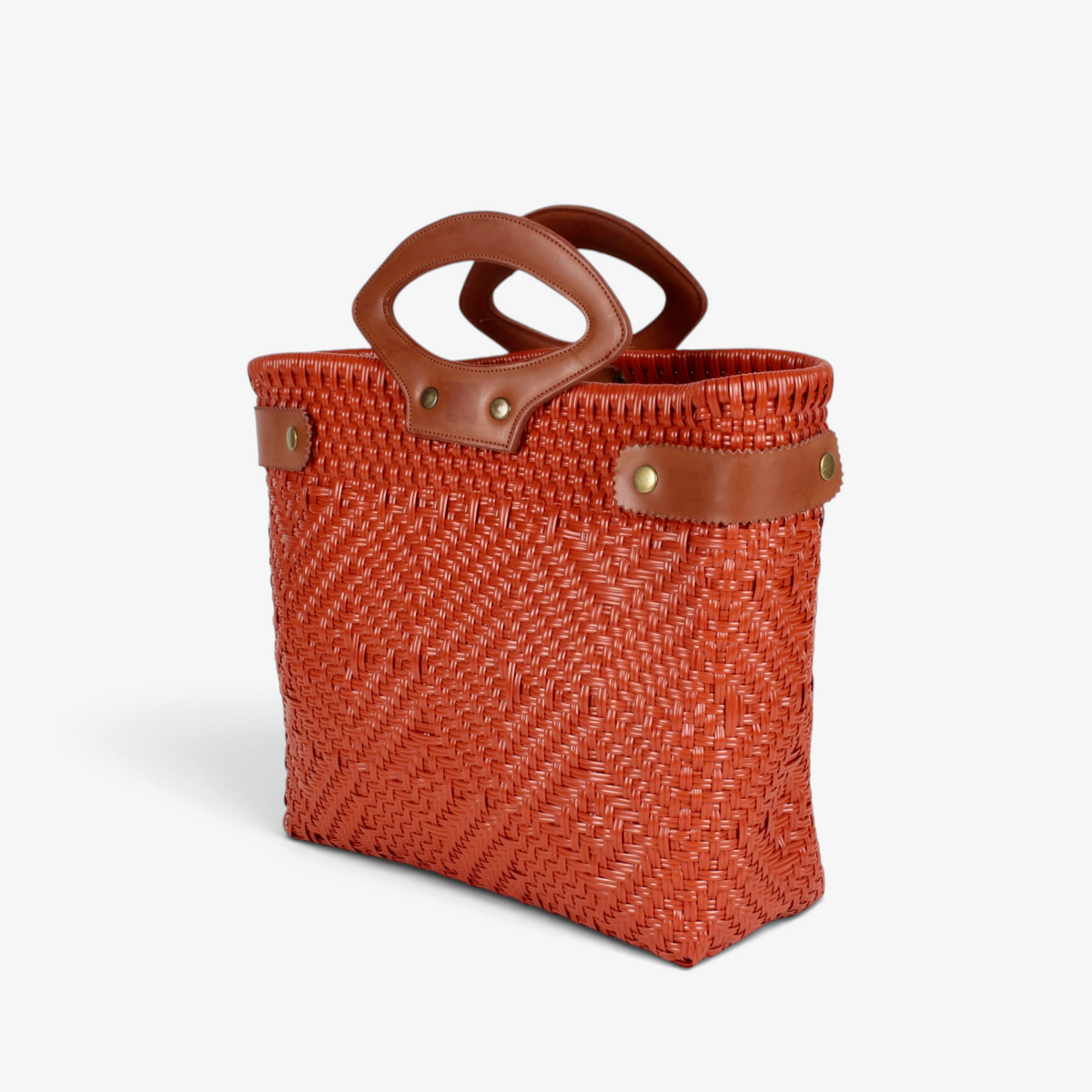 Burnt orange handwoven basket bag with leather handles and snap side straps, angled view