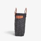 Side view of the charcoal gray woven basket bag showing its adjustable leather side strap