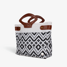 White and black patterned woven basket bag with brown genuine leather handles, angled view