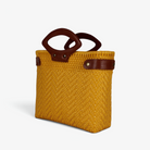 Mustard yellow handwoven tote with brown genuine leather handles and snap side straps, angled view