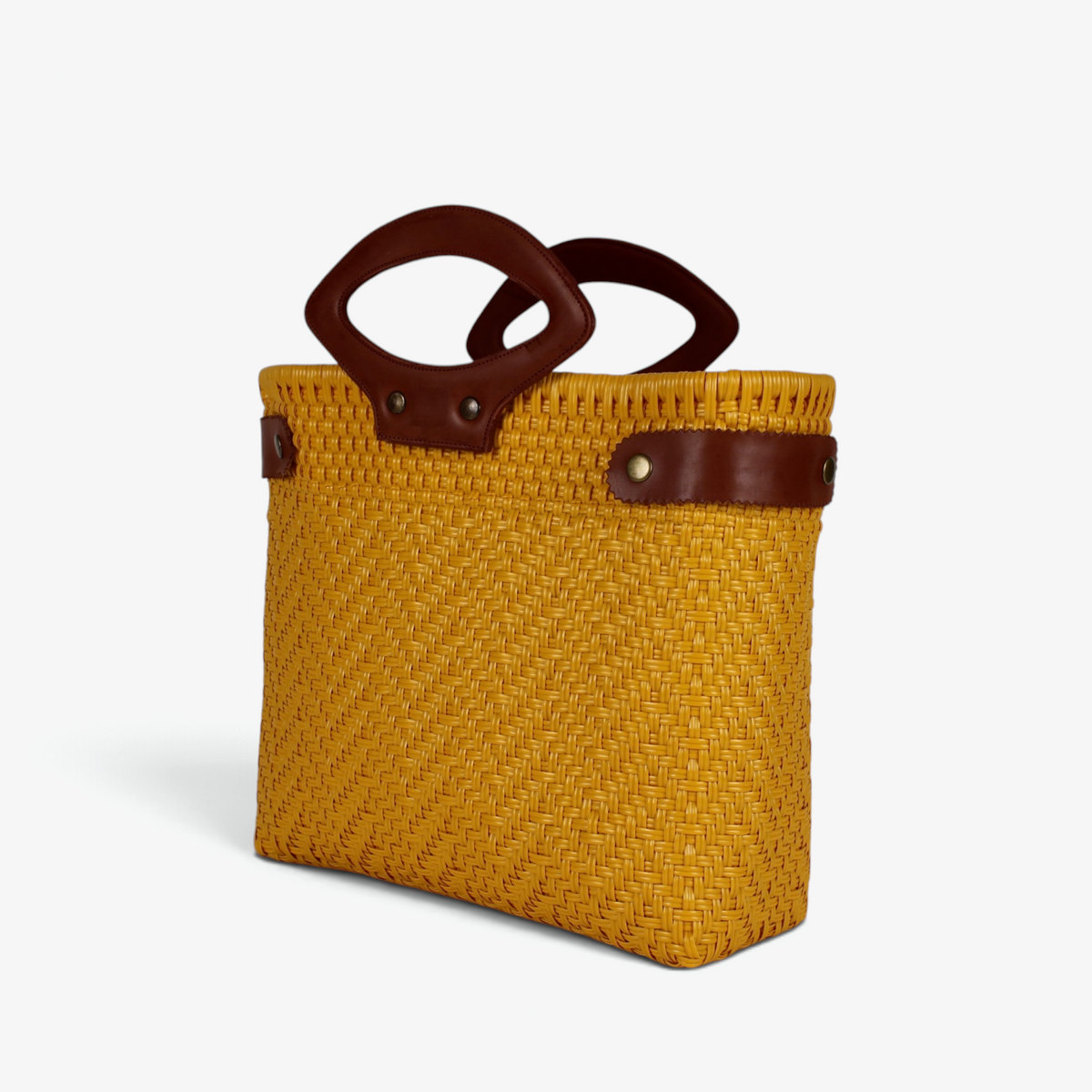 Mustard yellow handwoven tote with brown genuine leather handles and snap side straps, angled view