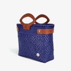 Royal blue handwoven basket bag with brown genuine leather handles and snap side straps, angled view