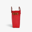 Side view of the red woven basket bag showing its adjustable leather side strap