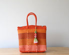 Orange woven bag with tassels on a wooden surface and light gray background