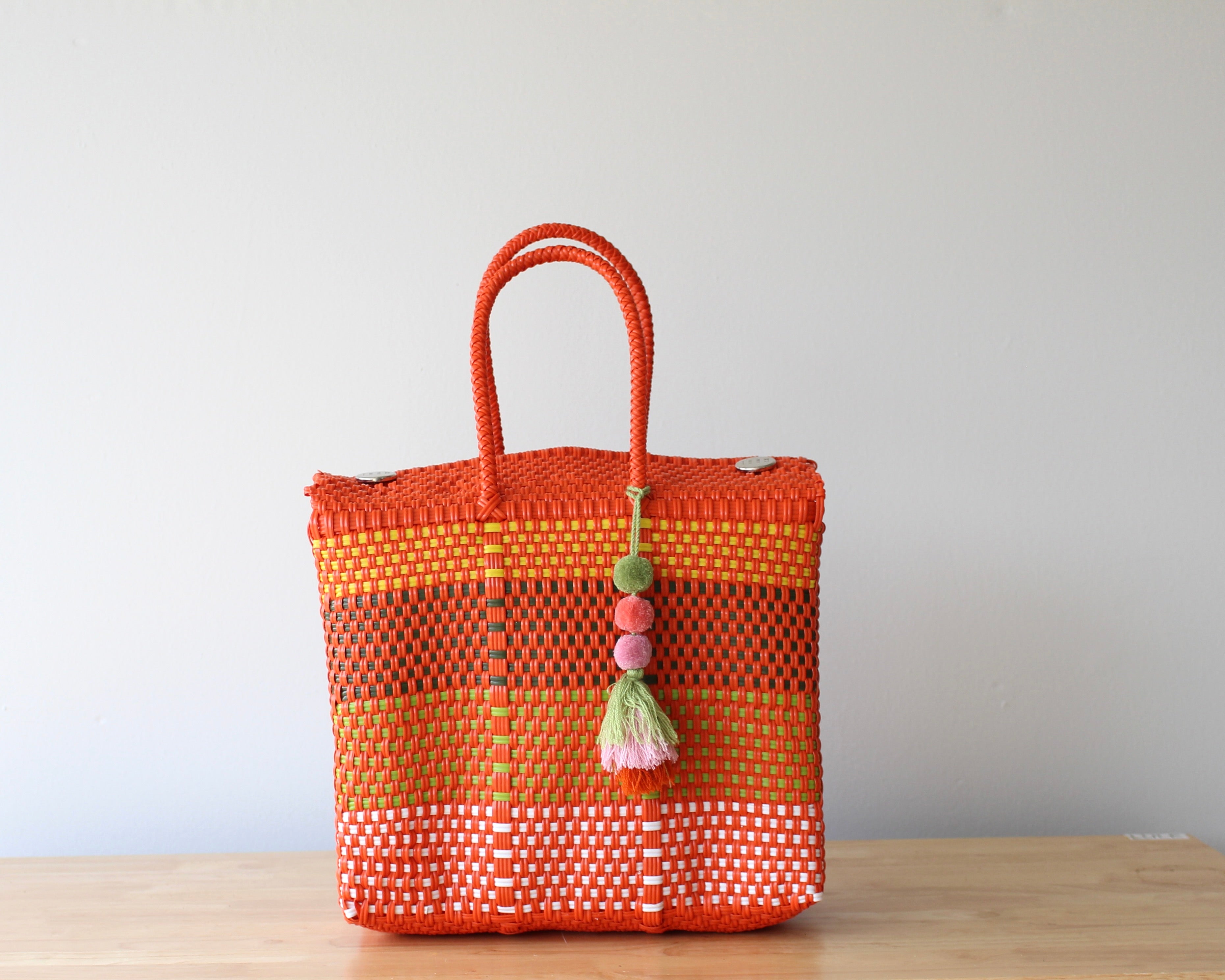 Orange woven bag with tassels on a wooden surface and light gray background