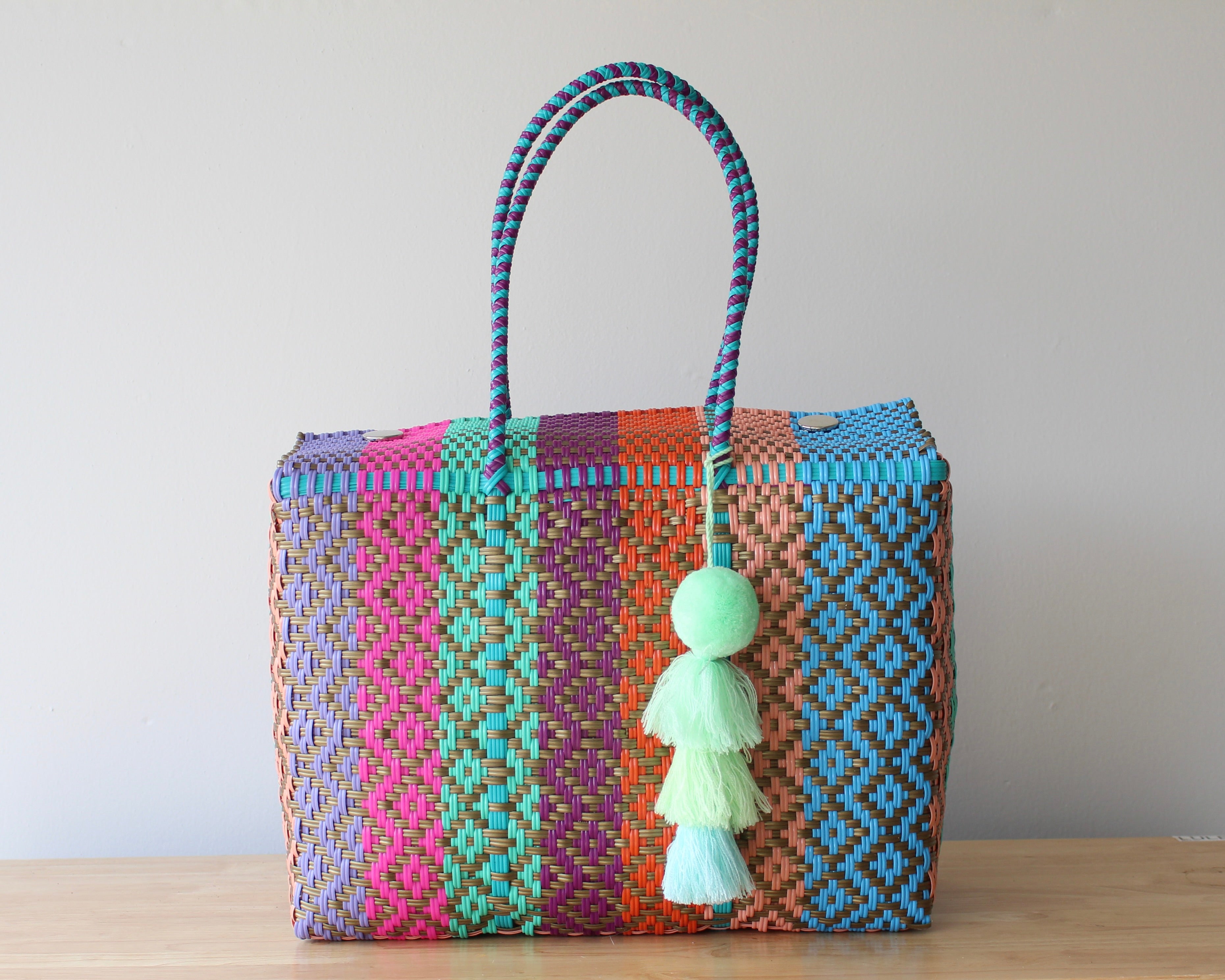 Colorful woven handbag with a tassel on a wooden surface and light gray background