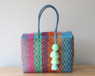 Colorful woven handbag with a tassel on a wooden surface and light gray background