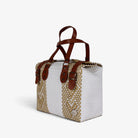 White and gold handwoven handbag with brown genuine leather handles and brass-tone hardware, angled view