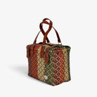 Earth tones handwoven handbag with brown genuine leather handles and brass-tone hardware, angled view