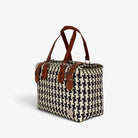 Black and cream houndstooth handwoven handbag with brown genuine leather handles and brass-tone hardware, angled view