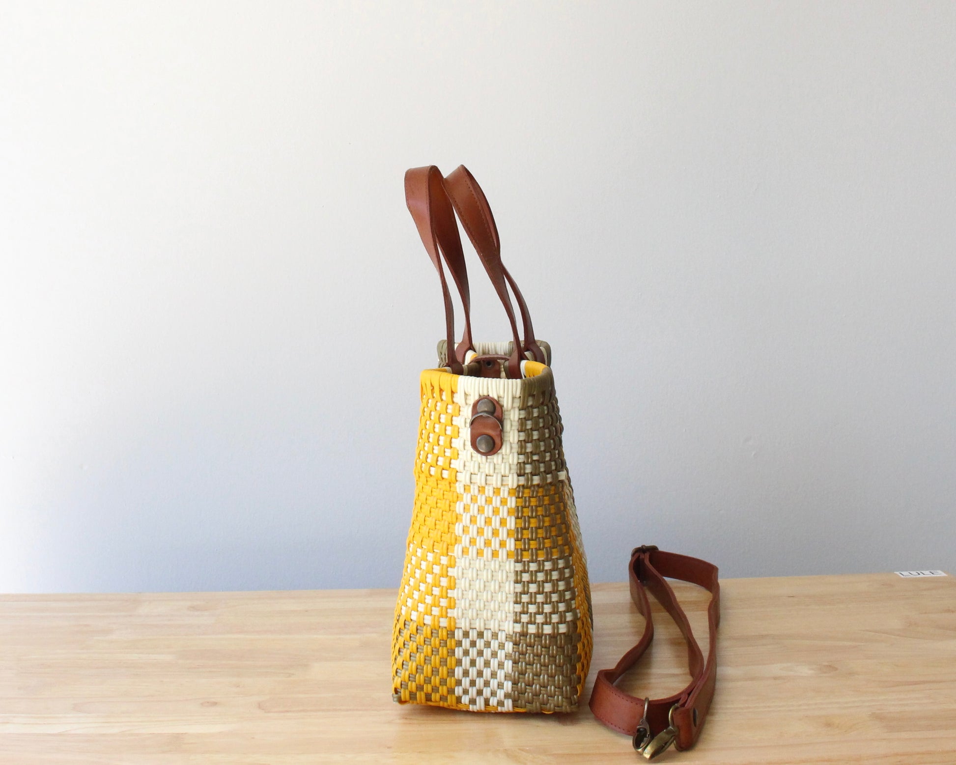 Close-up of the brown leather handles on a handmade recycled plastic purse, showcasing artisanal craftsmanship