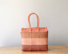 Woven tote bag with pink top handle on a wooden surface against a light gray background