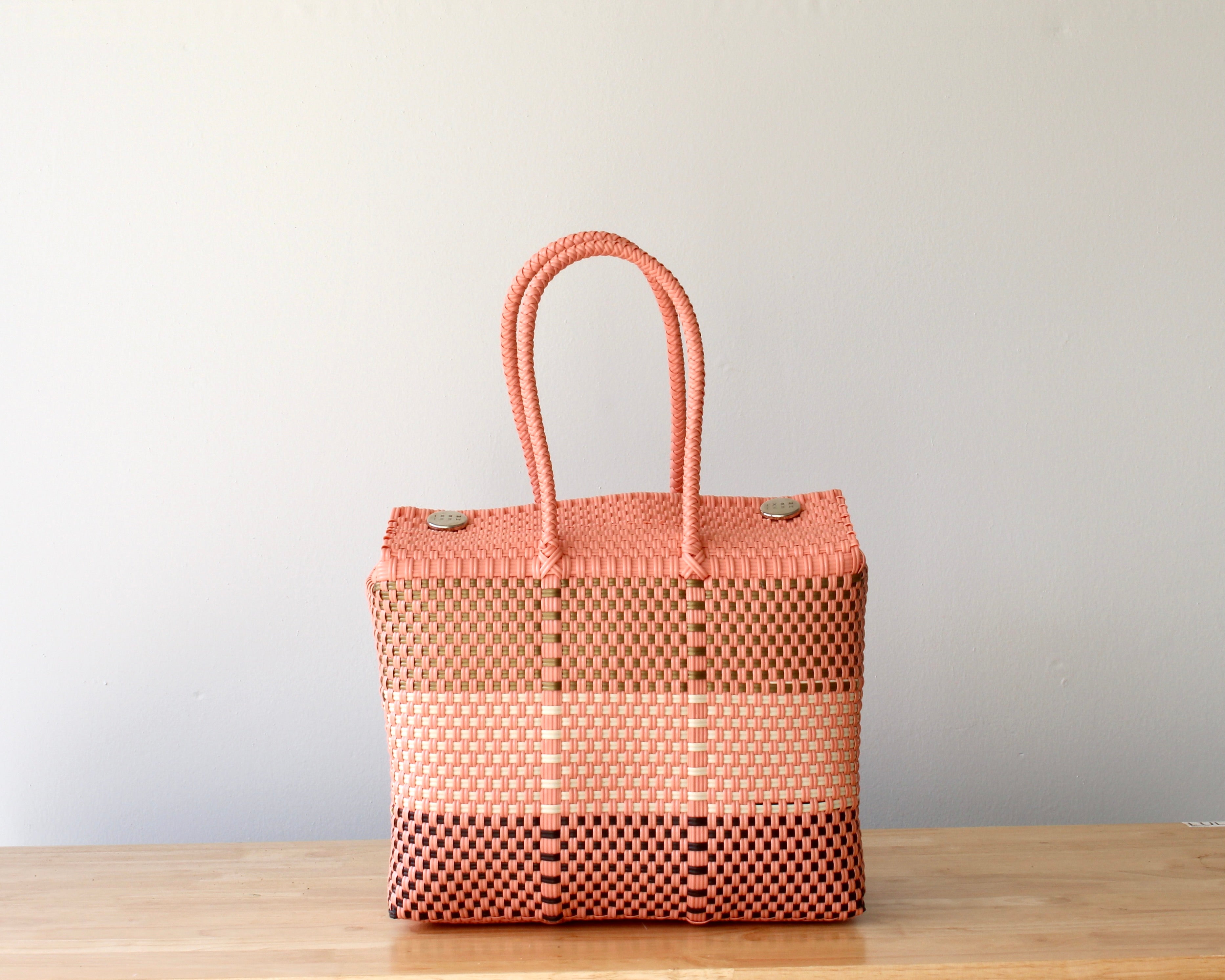 Woven tote bag with pink top handle on a wooden surface against a light gray background