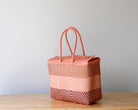 Woven pink bag on a wooden surface with a light gray background