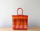 Orange woven basket on a wooden surface with a light gray background