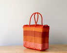 Woven orange bag with checkered pattern on a wooden surface and light gray background
