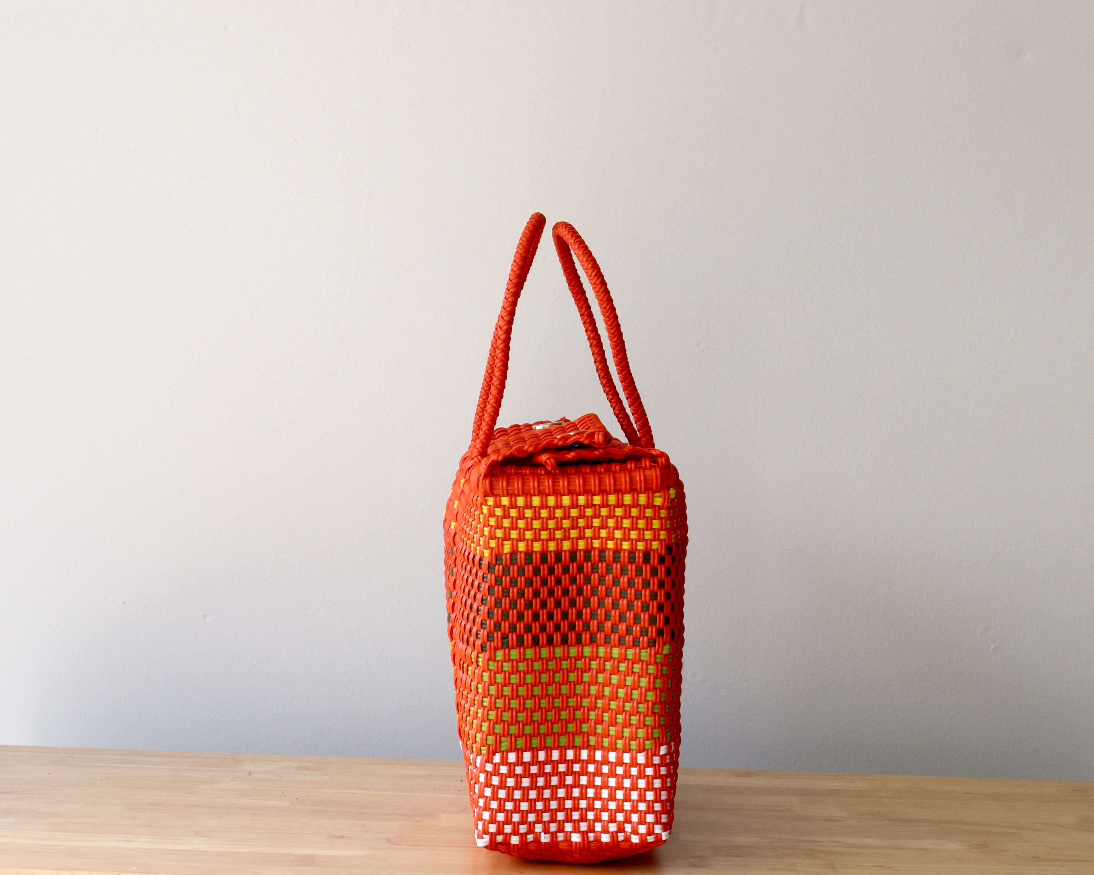 Orange woven bag on a wooden surface with a plain background