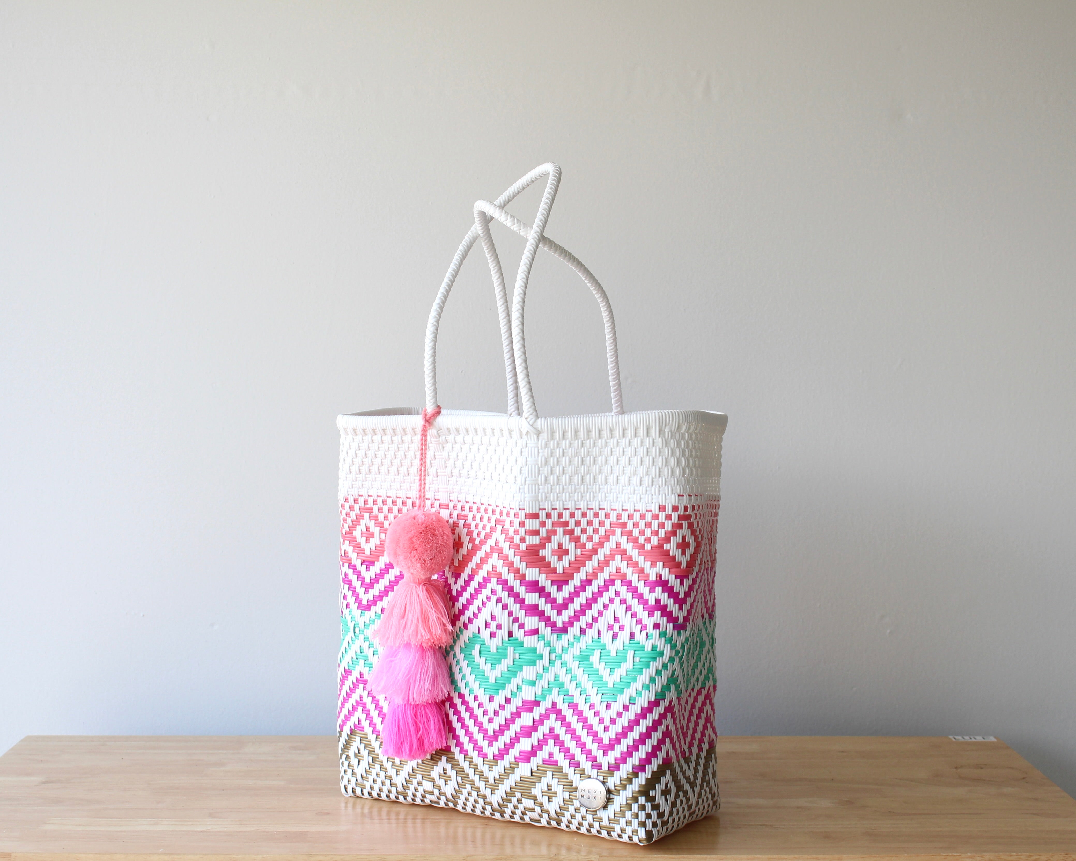 Angle view of boho woven tote in White, Coral , Pink & Aqua, with an artisan Heart Pom Pom— handmade in Guadalajara Mexico