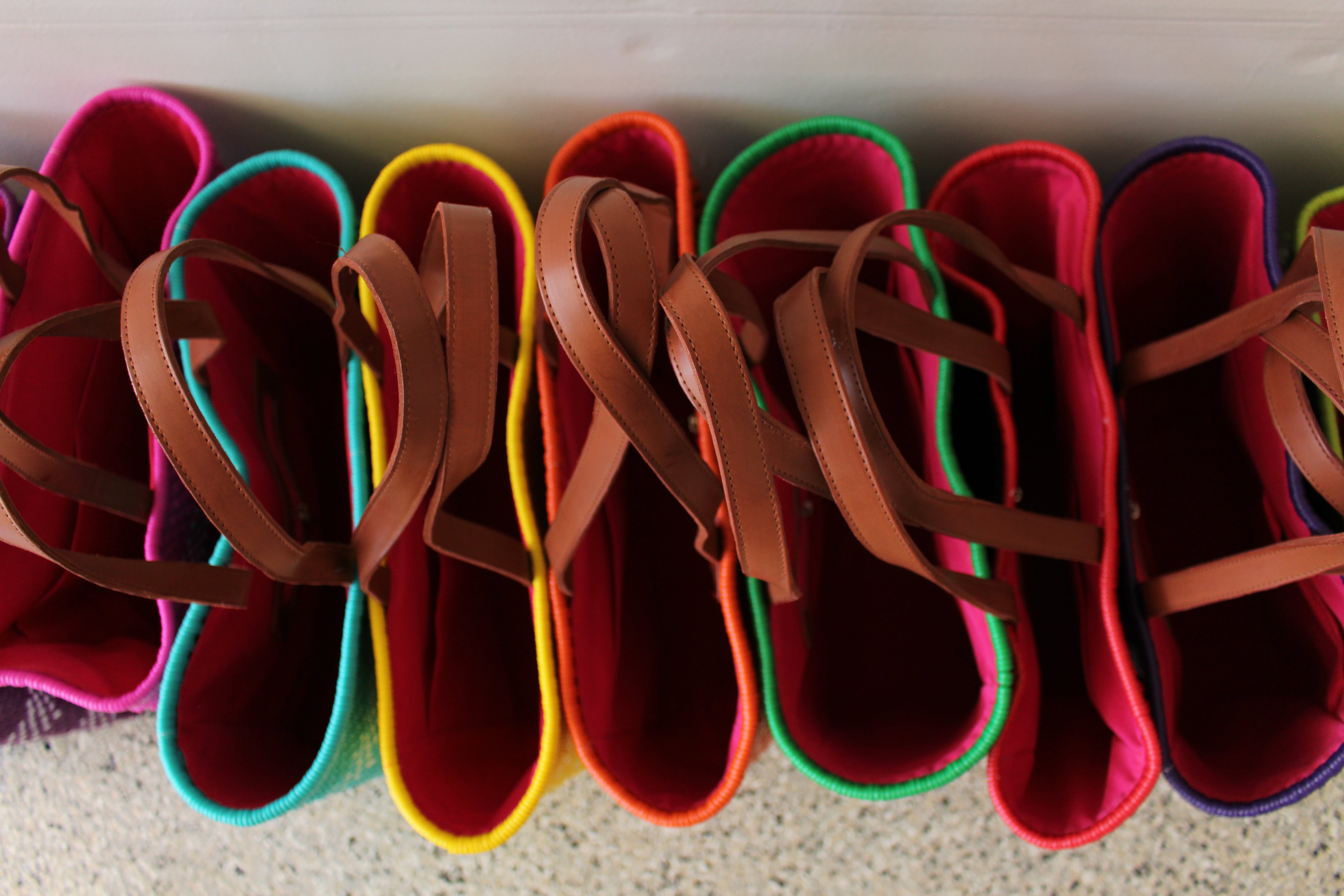 A row of colorful felt shoe trees with brown faux-leather straps, lined up on a speckled floor. The shades include pink, teal, yellow, orange, green, and magenta.