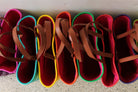 A row of colorful felt shoe trees with brown faux-leather straps, lined up on a speckled floor. The shades include pink, teal, yellow, orange, green, and magenta.