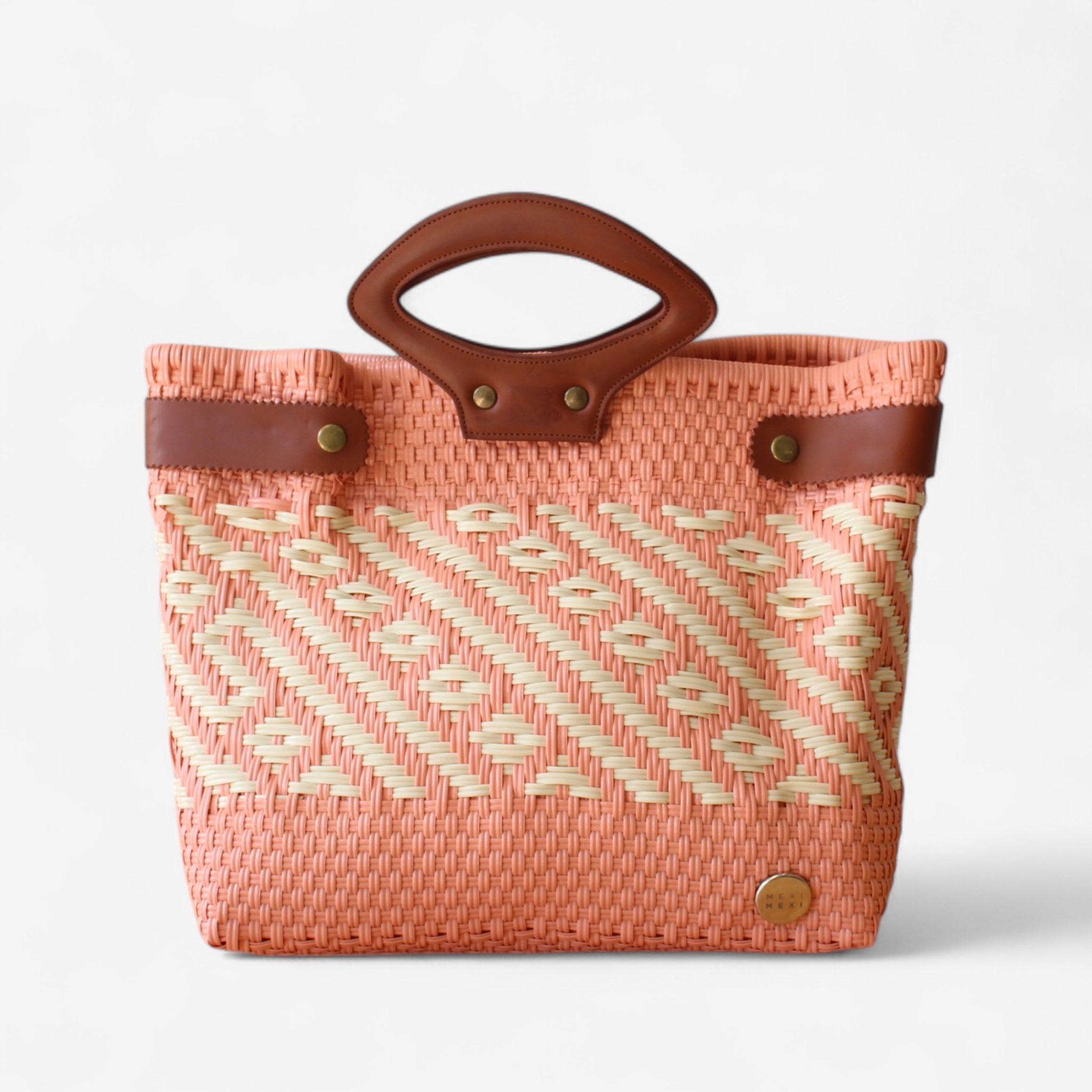 Handmade coral and cream woven tote bag with brown leather handles on a wooden table